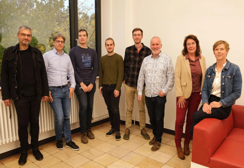 The members of the teaching advisory board are standing next to each other, with a woman sitting on the armrest of a red armchair on the far right.