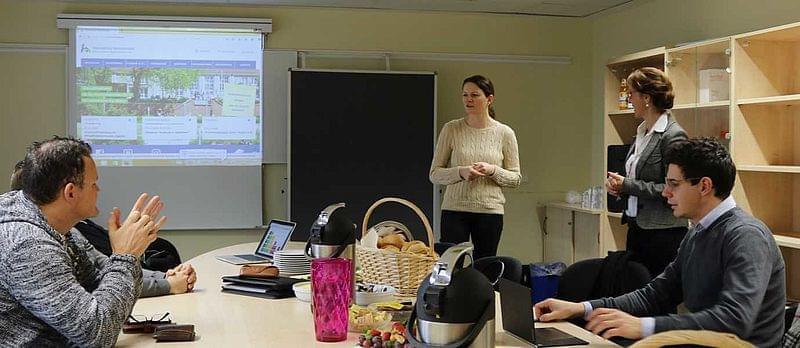 Personen an einem Tisch. Im Hintergrund eine Projektion der Hochschule-Website