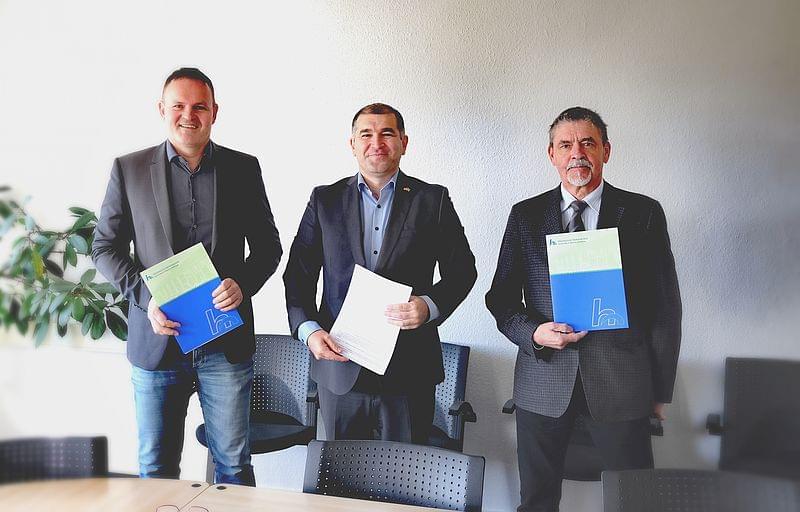 Prof. Wagner, Herr Ahmadow und Herr Herfurth stehen nebeneinander. Jeder hält eine Mappe.