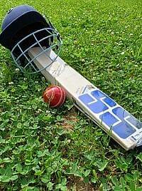 Cricket-Schläger, -Ball und -Helm liegen auf grünem Rasen