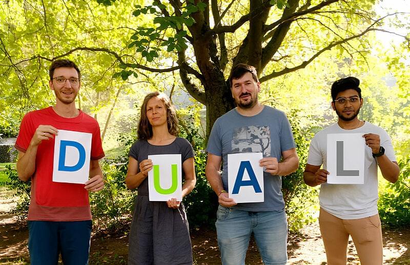 vier Mitarbeiter mit dem Wort dual auf Schildern
