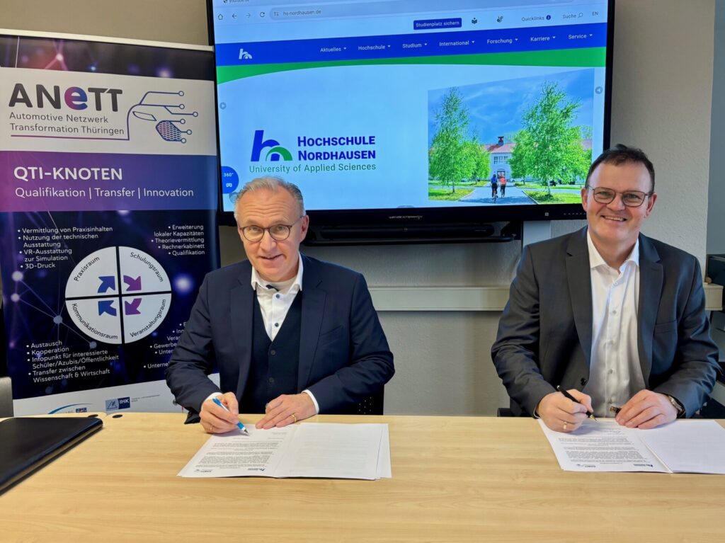 2 men sign a contract at a table and smile