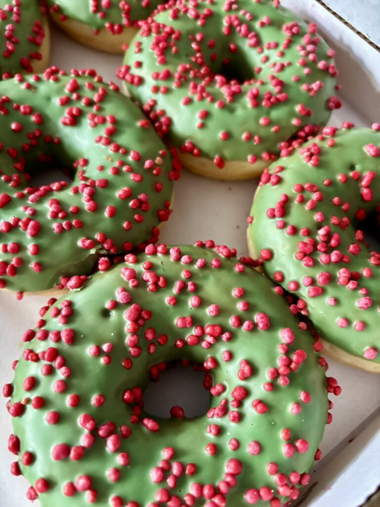 Mehrere Donuts mit grünem Zuckerguss und roten Zuckerperlen auf einem Tablett.