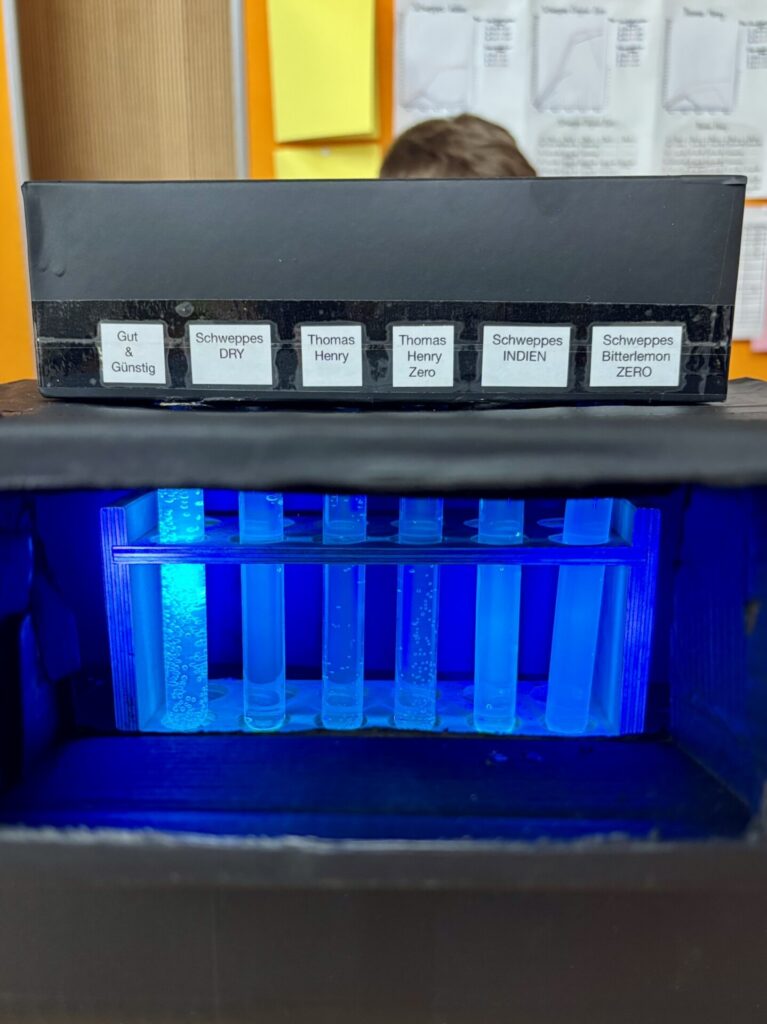 Ein blau leuchtendes Laborgerät mit mehreren Röhrchen, im Hintergrund eine Person.