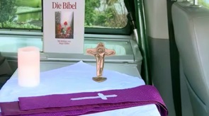 Caption:Confession mobile interiorAlt-Text:View into the interior of the confession mobile; table with a lit candle and a Bible.