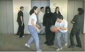 Während sich die Spieler den Ball zuwerfen, läuft eine als Gorilla verkleidet Person durch die Spielergruppe.