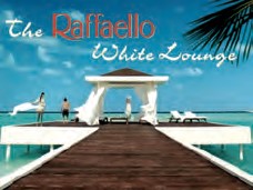 The picture shows a summery beach scene with a dark wooden walkway leading to a white pavilion with billowing curtains. Bright blue water and a light-coloured sandy beach under a blue sky can be seen in the background. People in light-coloured clothing can be seen on the jetty and by the pavilion. The title „the Raffaello White Lounge“ is written in curved lettering at the top. Palm leaves protrude into the picture in the top right-hand corner.